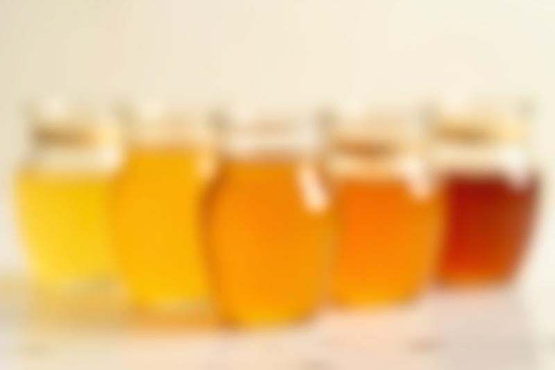 Close-up of several jars of honey showing different hues and consistencies, highlighting natural variations.